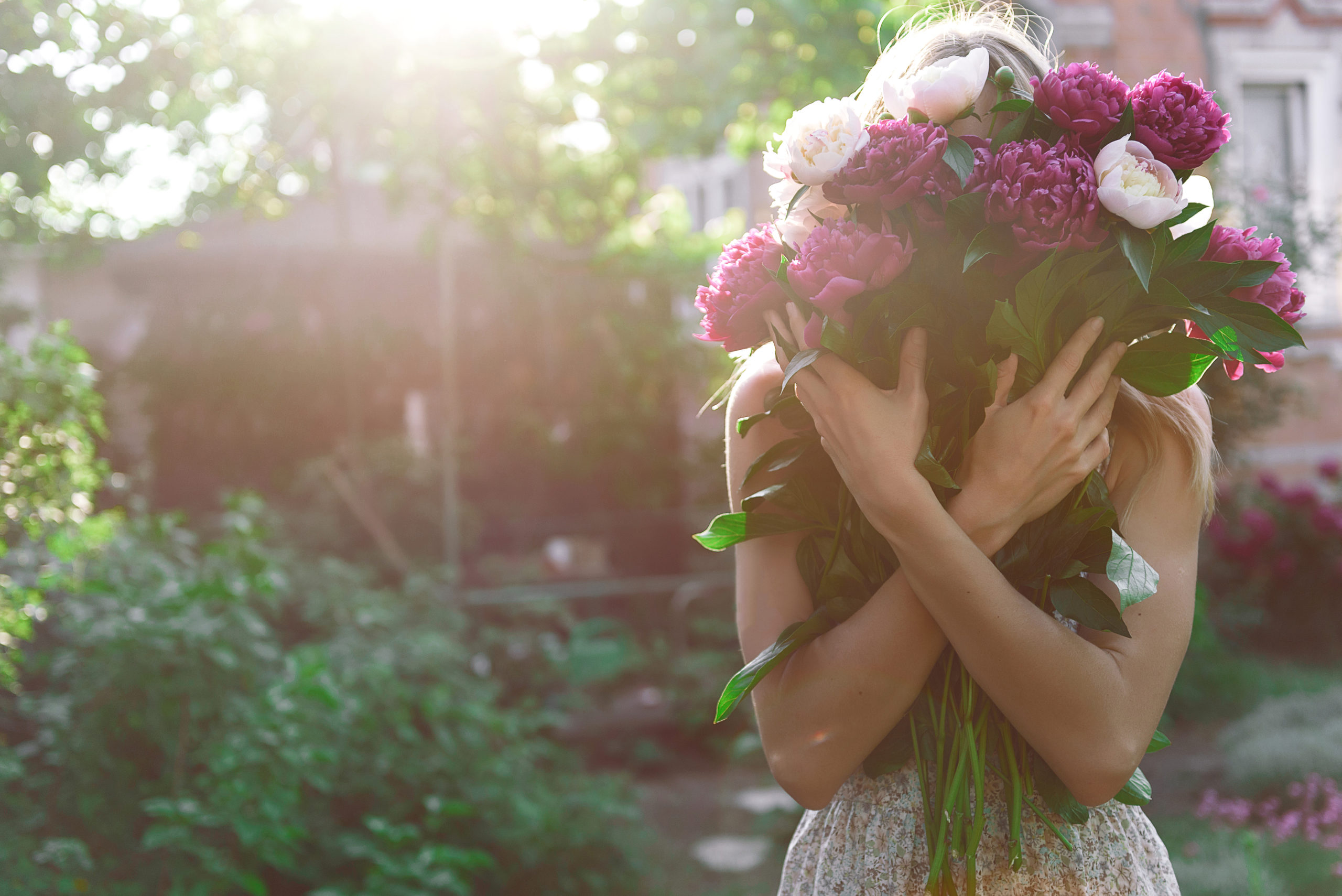 girl in the garden with a big bouquet of peonies in hands at sun